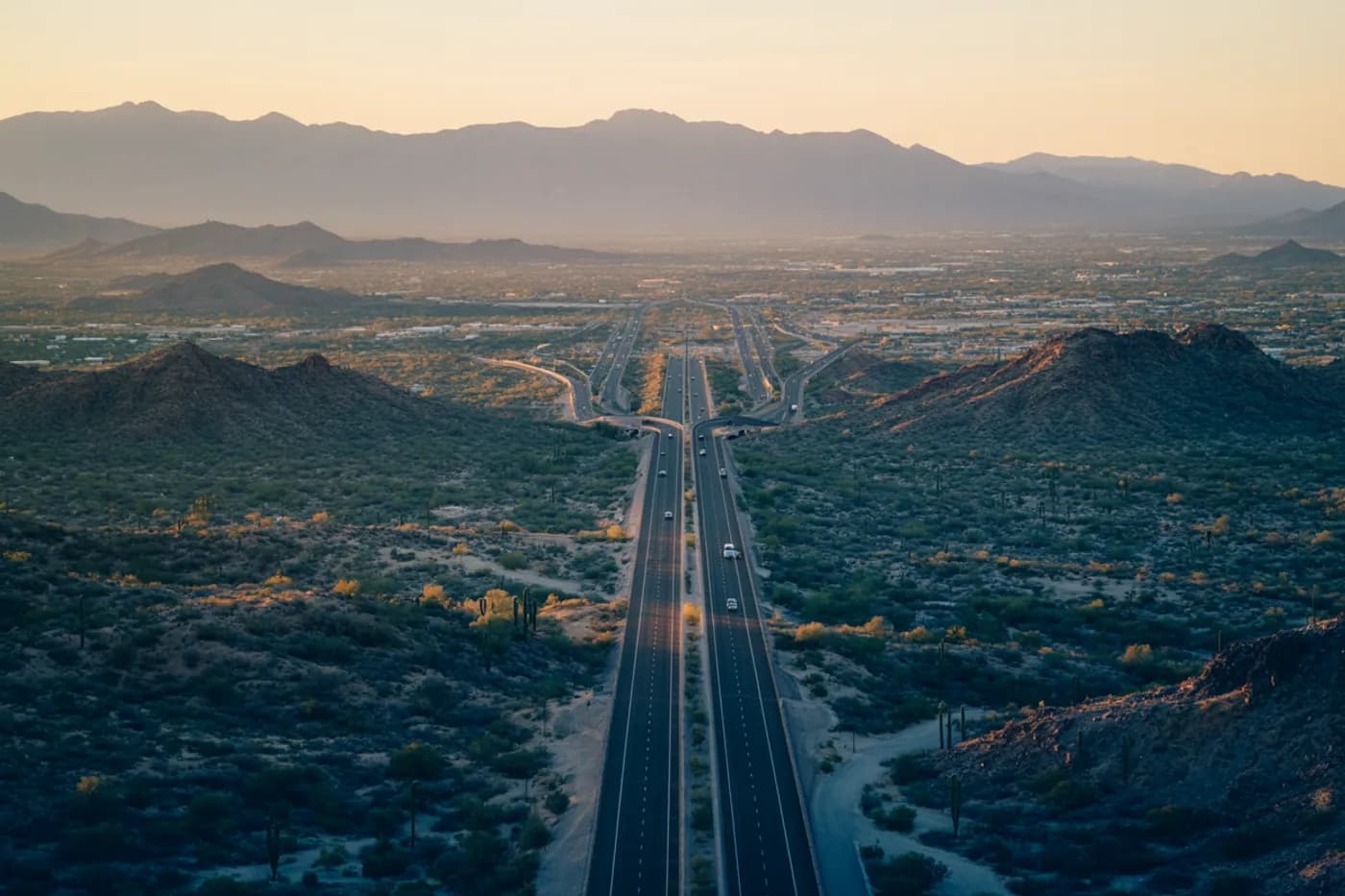 Arizona desert highways radiating across the Sonoran valley toward distant mountains at golden hour