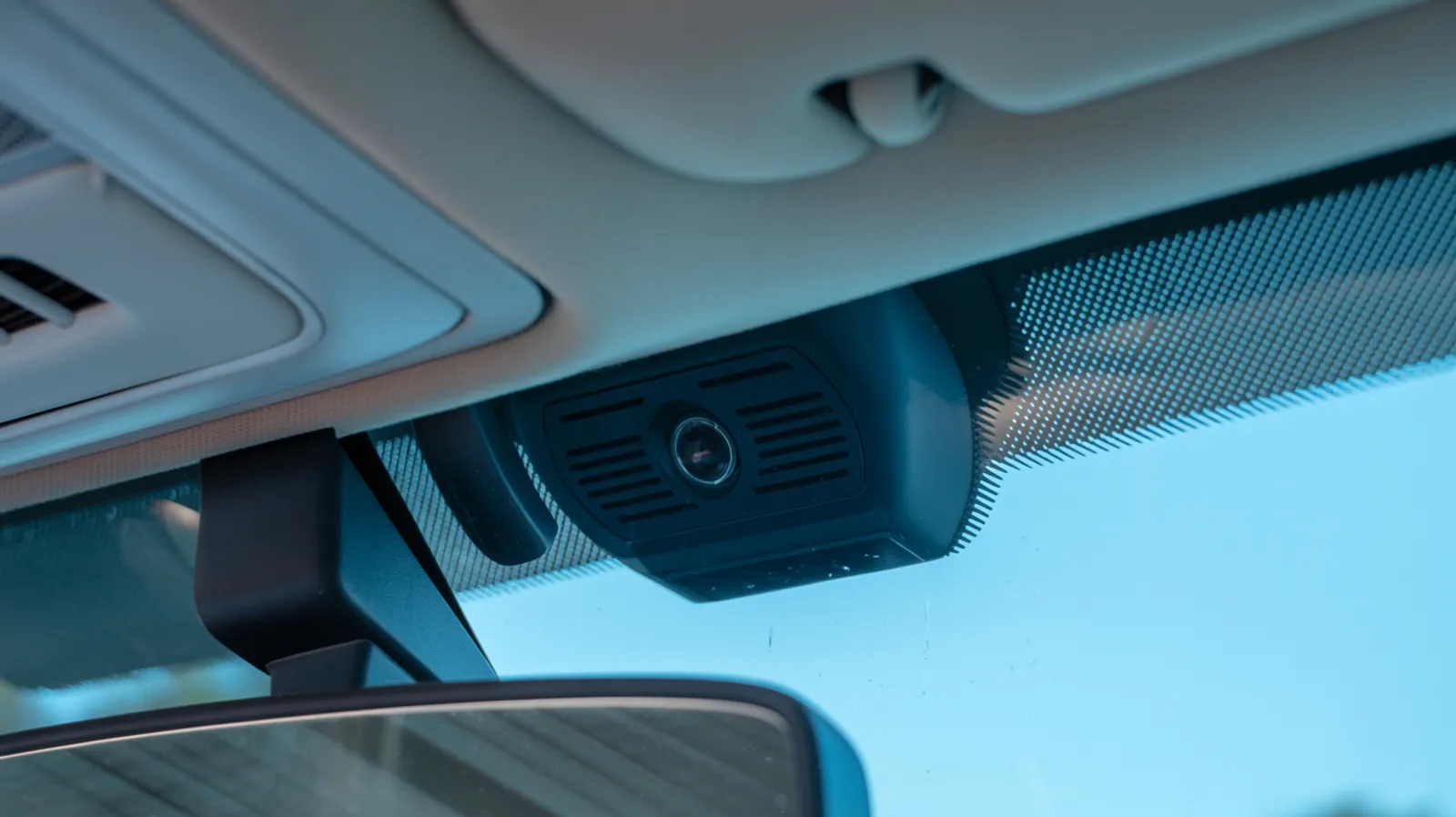 Close-up of the sensor housing and camera bracket mounted behind the rear-view mirror on a modern windshield